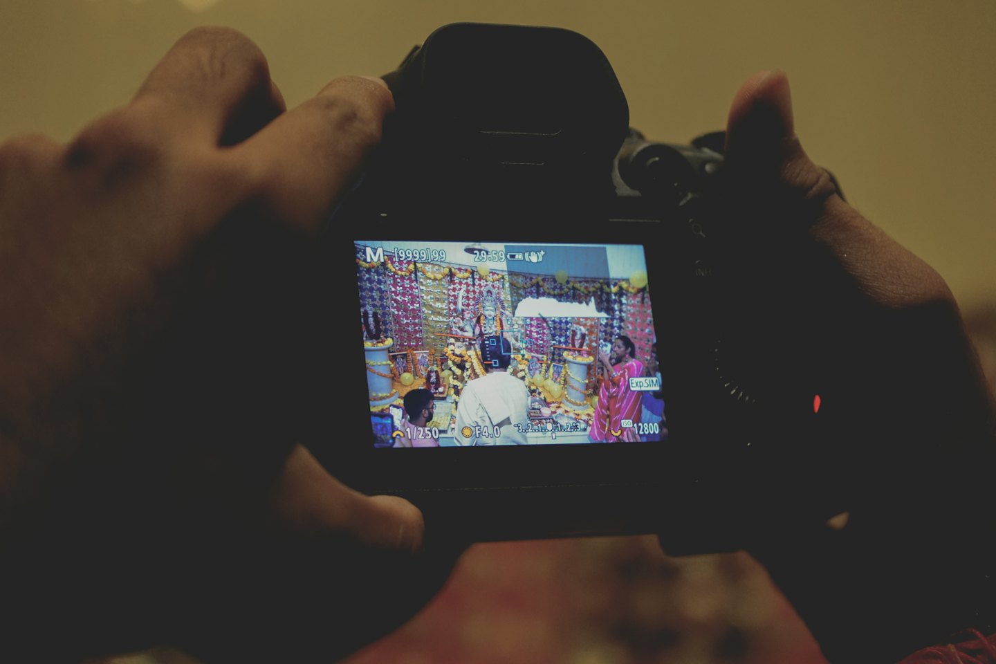 Hands holding a digital camera displaying a decorated indoor event.